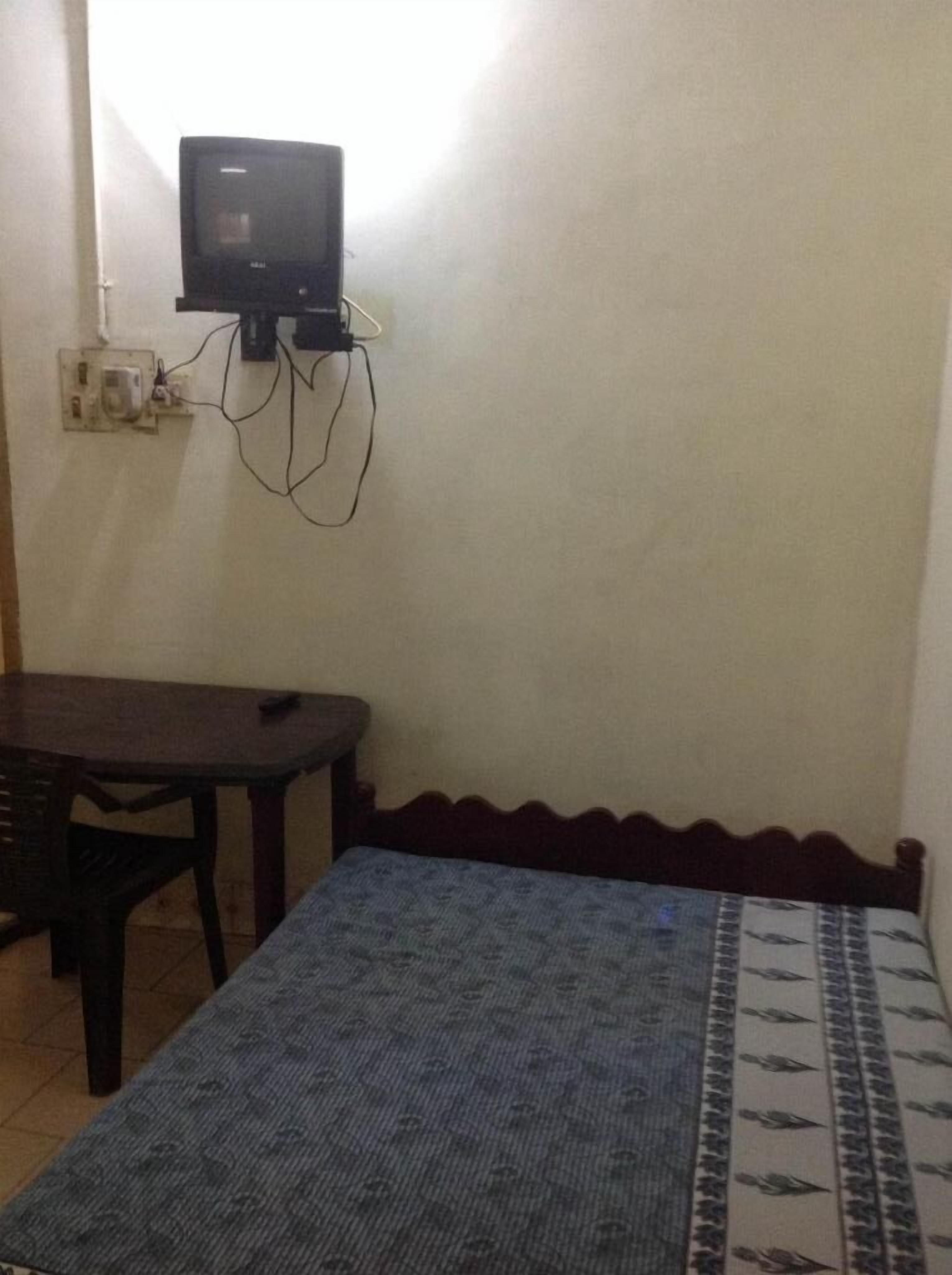 A small room with a bed, a table, and a television mounted on the wall.