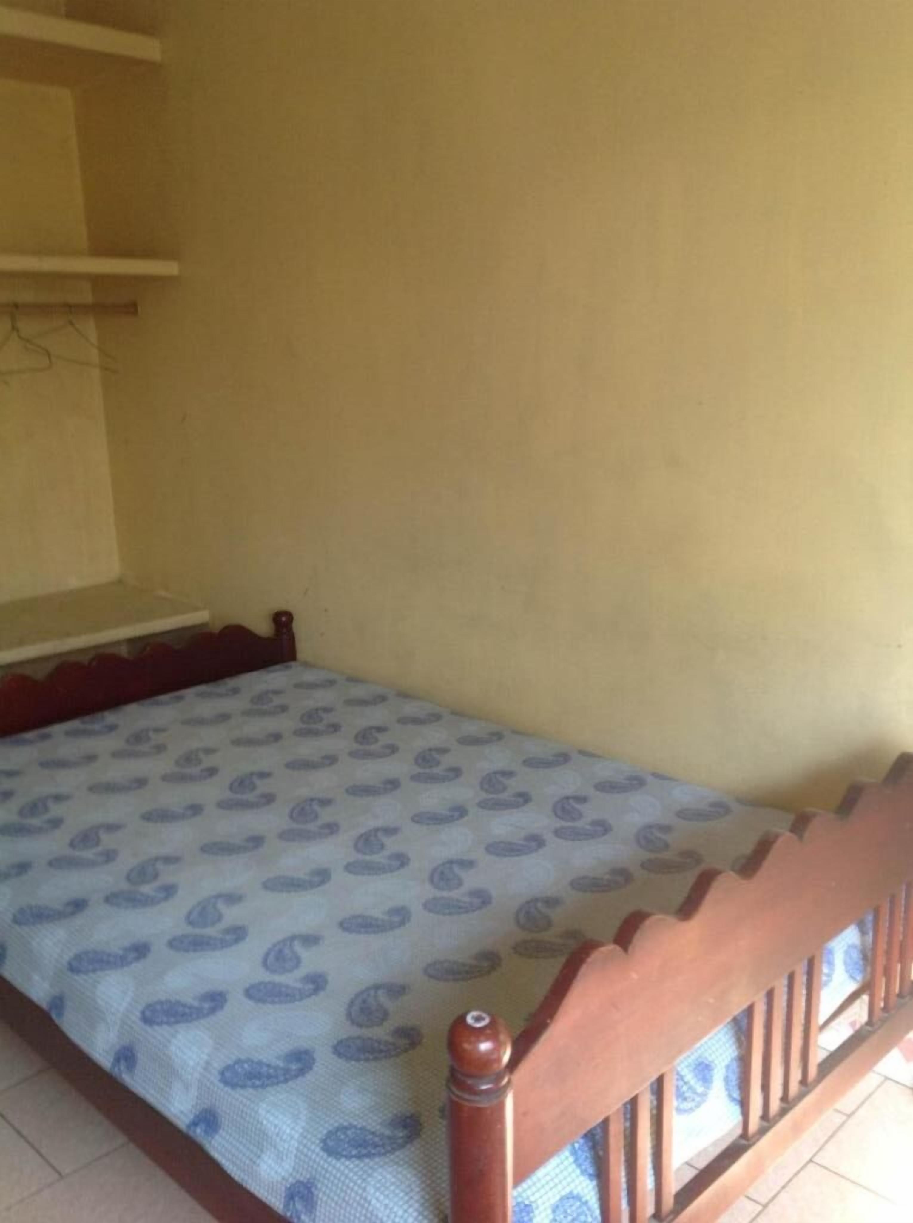 A single bed with a patterned bedspread in a room with plain yellow walls and a wooden headboard.