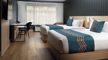 A hotel room with two beds, a desk, and a TV.