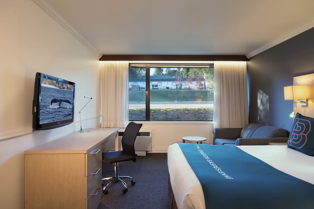 Ein Hotelzimmer mit Bett, Schreibtisch, Stuhl und Fernseher an der Wand.