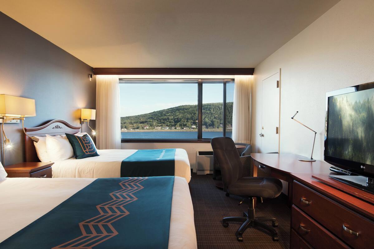 Ein Hotelzimmer mit zwei Betten, einem Schreibtisch, einem Fernseher und Blick auf einen See.