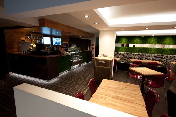 Un restaurant moderne doté d’un bar, de tables en bois et de chaises rouges.