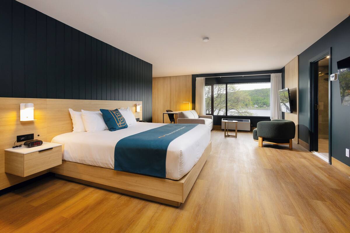 Ein modernes Hotelzimmer mit einem großen Bett, Nachttischen, einem Schreibtisch und Blick ins Freie.