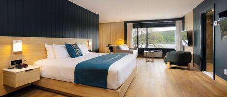 A modern hotel room with a large bed, bedside tables, a desk, and a view of the outdoors.