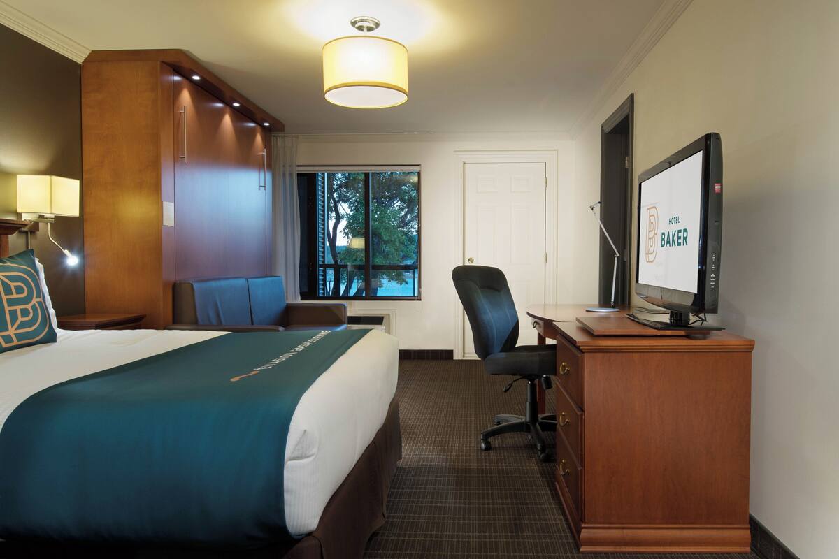 Ein Hotelzimmer mit einem Bett, einem Schreibtisch mit Computer, einem Sessel und einem Fernseher.
