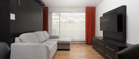 Una sala de estar moderna con un sofá gris, un televisor sobre un mueble negro y piso de madera.