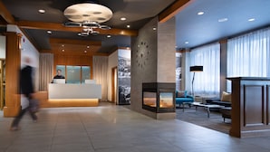 A modern lobby with a fireplace, seating area, and a receptionist desk. - Hôtel Baker (Gaspé)