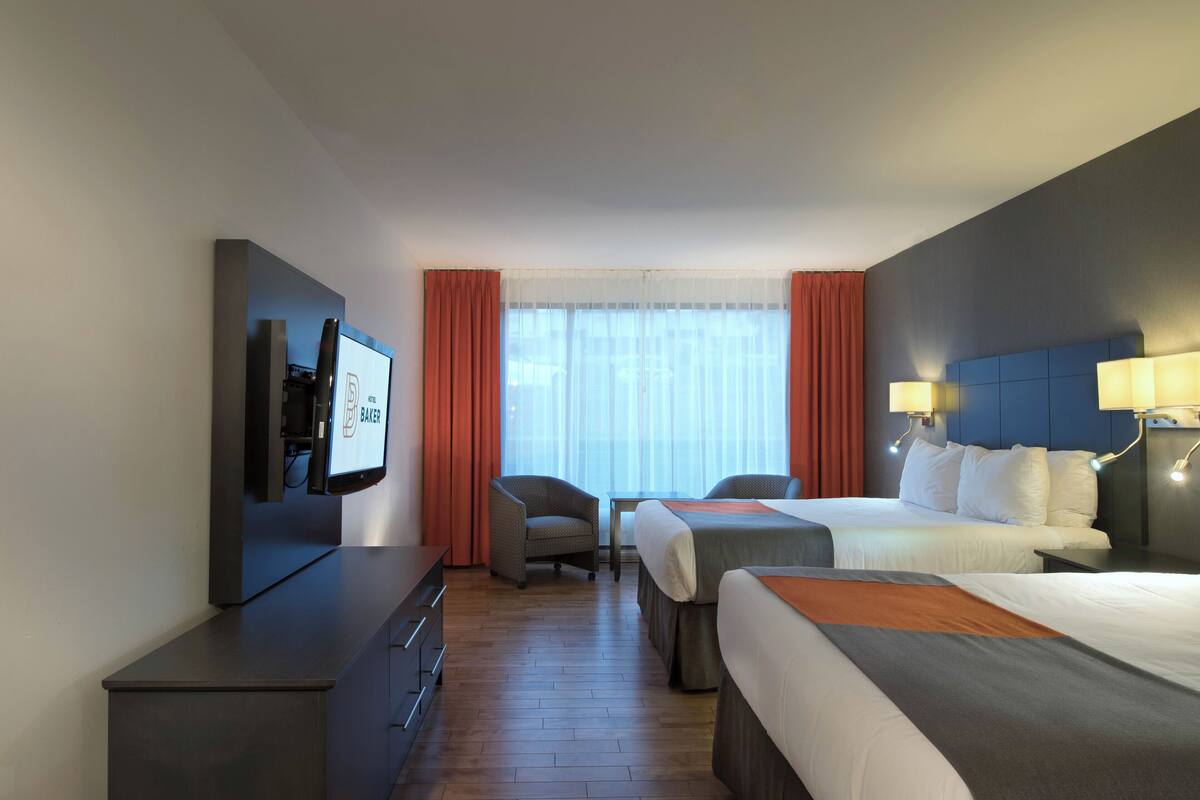 Ein Hotelzimmer mit Fernseher, zwei Betten, einem Schreibtisch und einem Sessel.