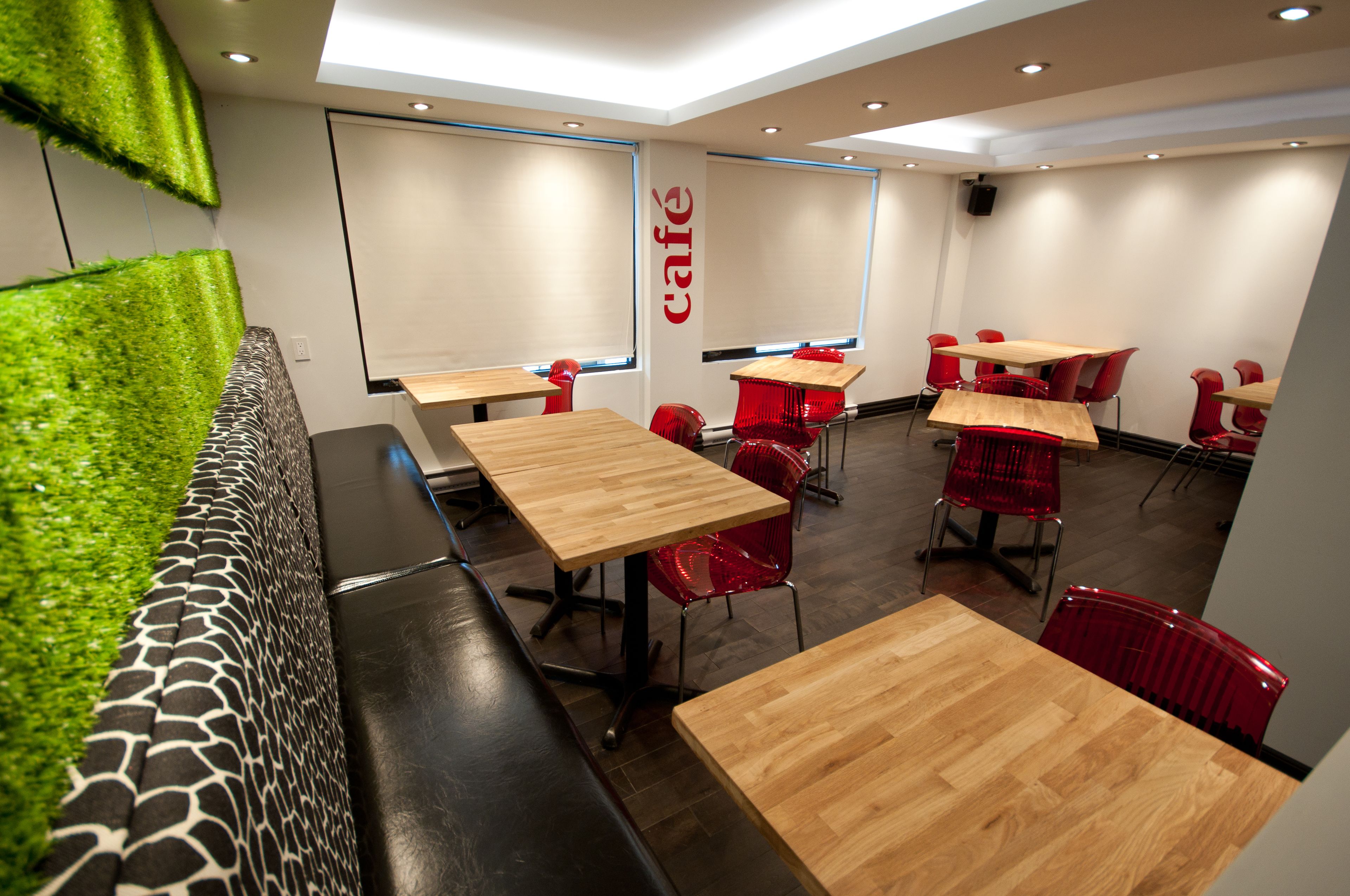 A modern café interior with wooden tables and red chairs, a green wall feature, and a 'café' sign on the wall.