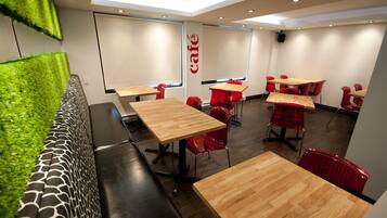 A modern café interior with wooden tables and red chairs, a green wall feature, and a 'café' sign on the wall.