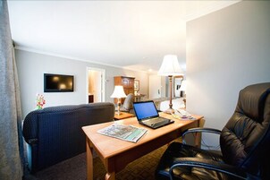 Quarto de hotel com escrivaninha, laptop, cadeira, luminária e televisão na parede.
