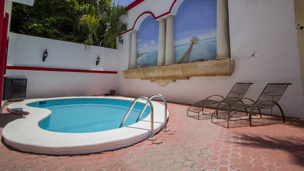 A swimming pool with a white and red tiled deck, a mural of a beach scene, and two metal chairs. - Hotel El Español Centro Histórico (Mérida)