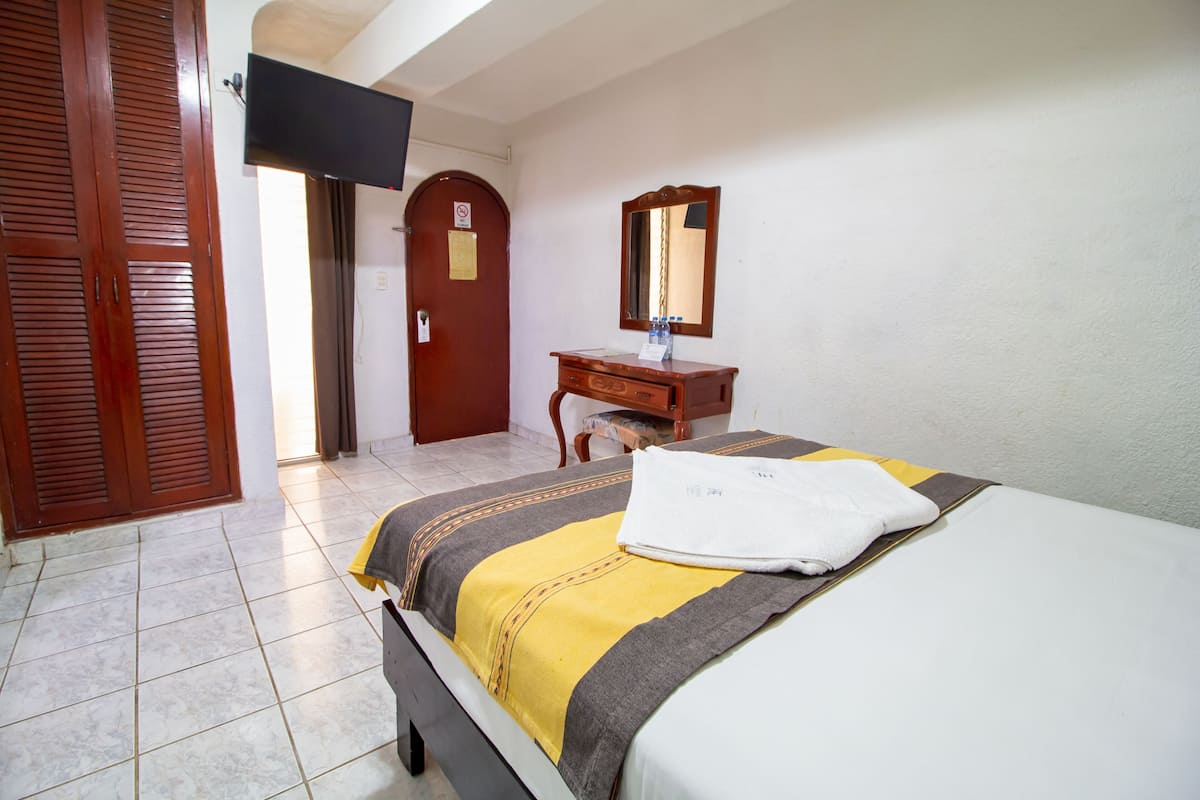 Une chambre d’hôtel avec un lit, une commode en bois, un miroir et un téléviseur fixé au mur.