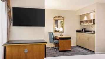 A hotel room with a bed, a desk, a chair, a TV, a mirror, a kitchenette, and a patterned carpet.