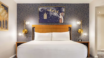 Una cama bien tendida con un cabecero de madera, dos mesitas de noche con lámparas, y una pared con un diseño geométrico y un cuadro enmarcado.