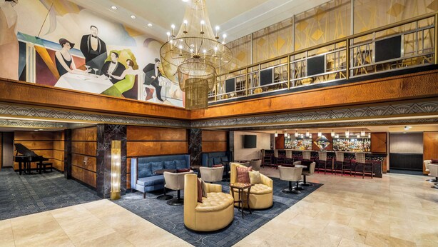 Um hall amplo com um lustre imponente, um piano, áreas de estar confortáveis e um bar com diversas garrafas.