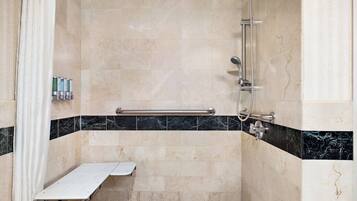 Una ducha a nivel con azulejos color beige, un borde de mármol negro y beige, una barra de apoyo y un cabezal de ducha.