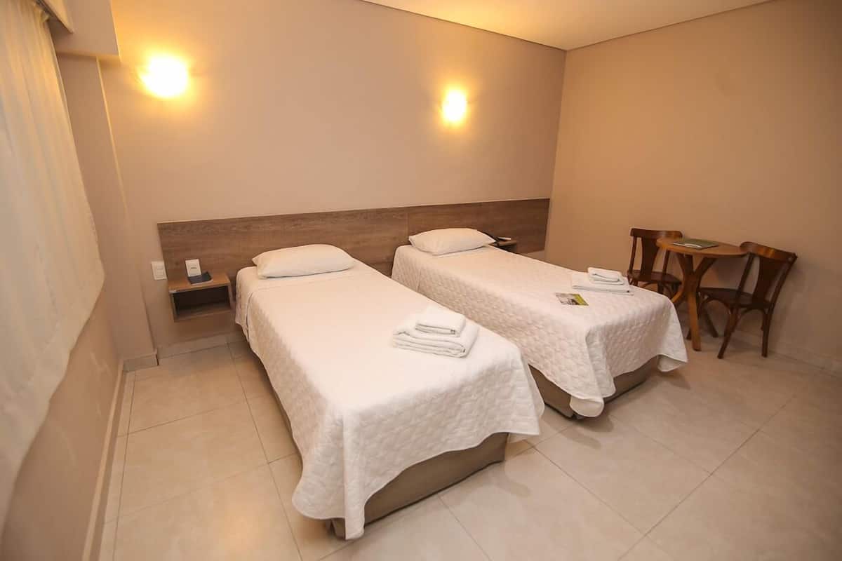 A hotel room with two single beds, a small table, and a chair.