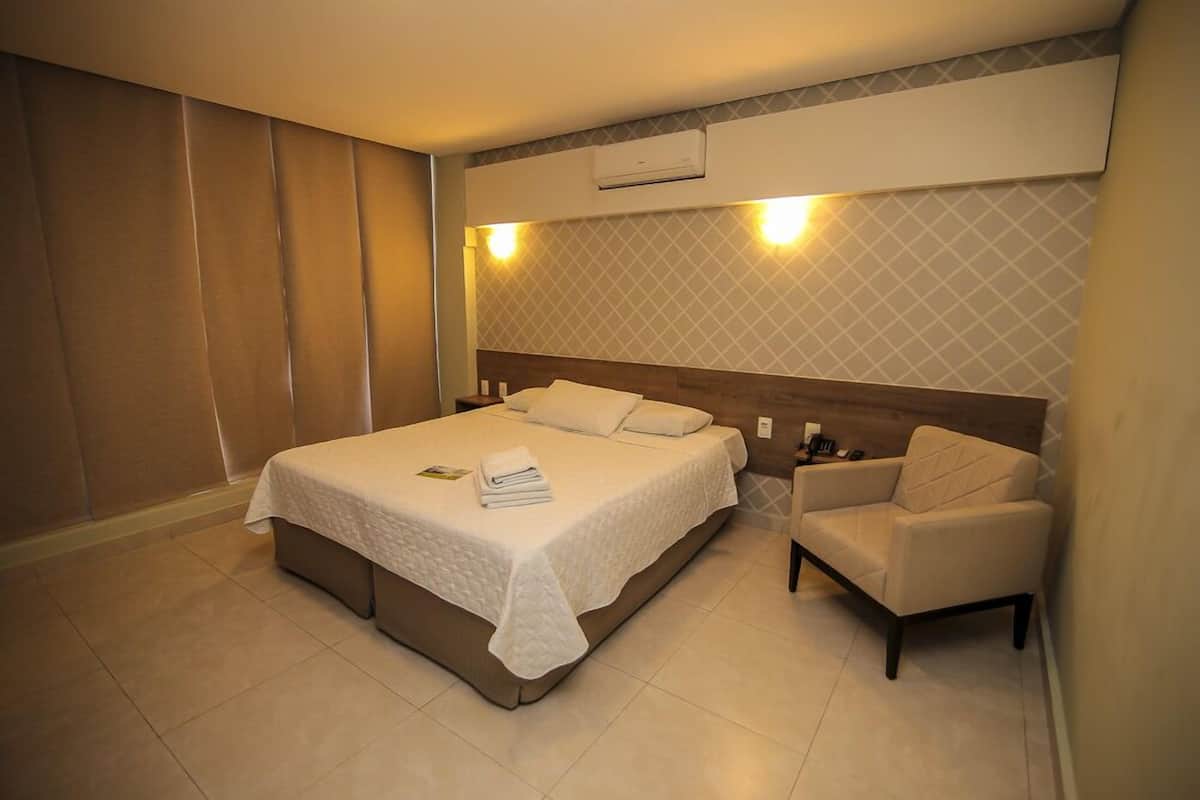 A hotel room with a bed, a chair, and a wall-mounted air conditioner.