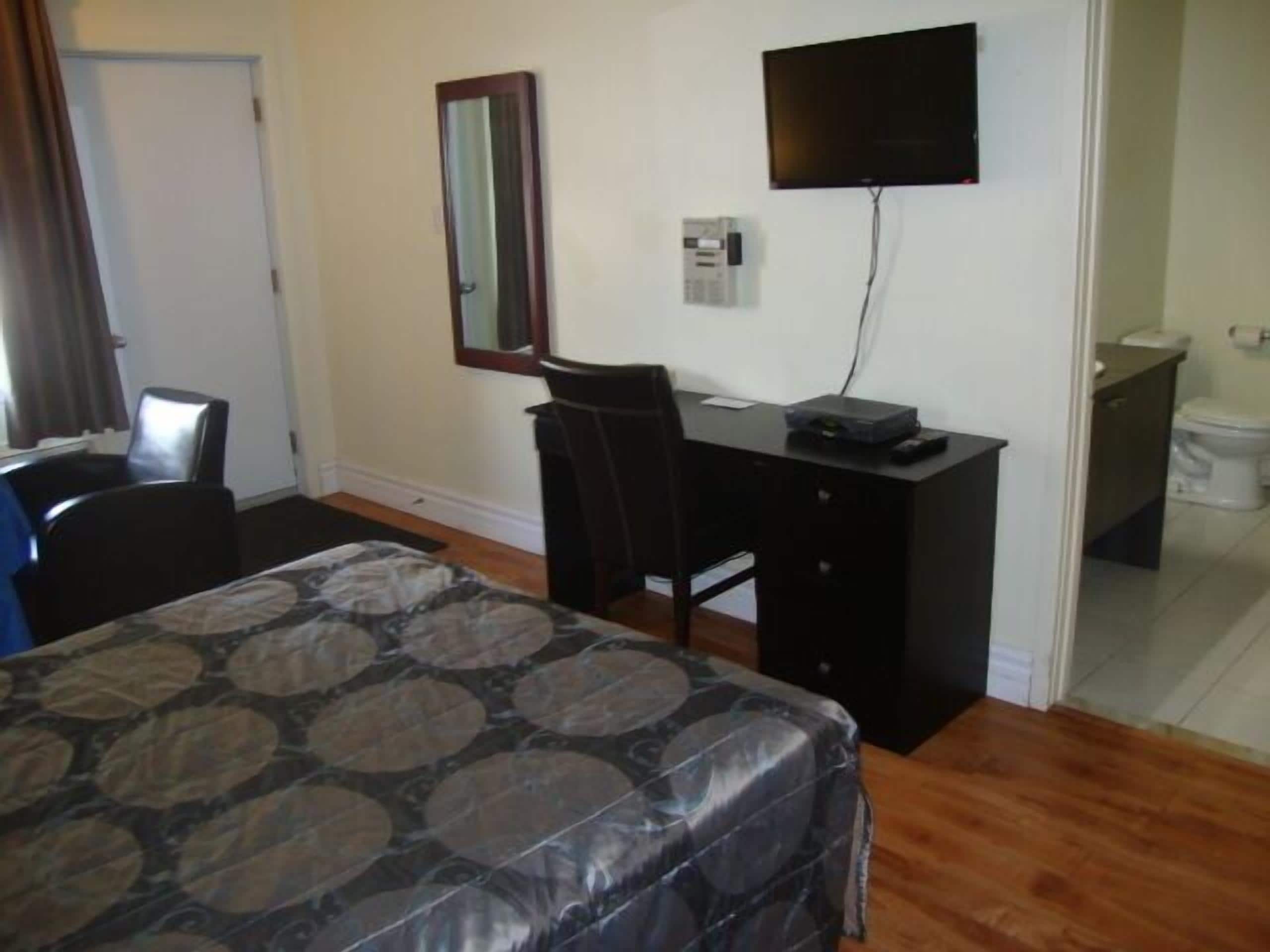 A bedroom with a bed, a desk, a chair, a television, and a bathroom.
