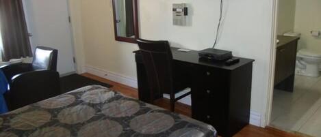 A bedroom with a bed, a desk, a chair, a television, and a bathroom.