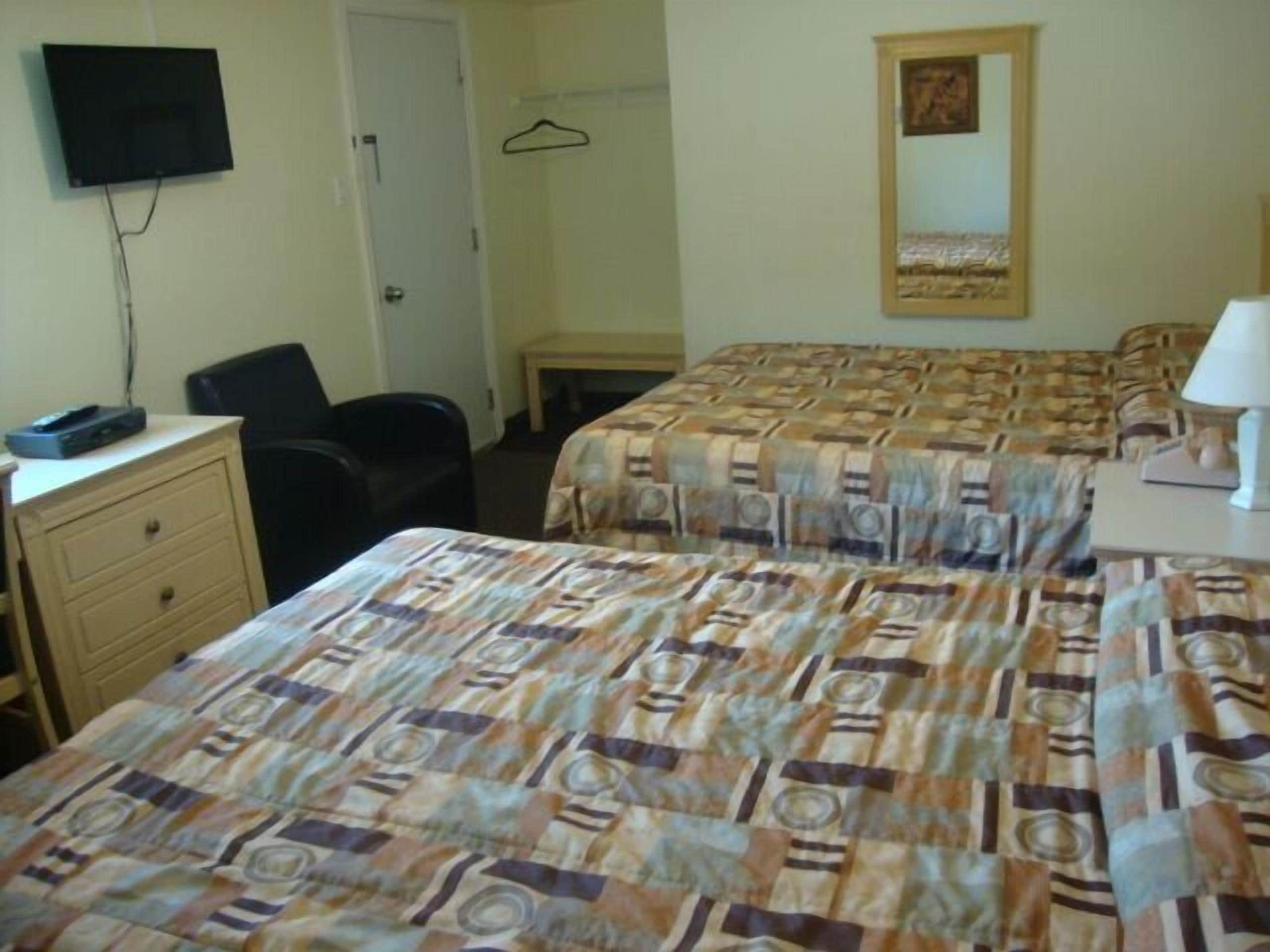 A hotel room with two beds, a desk with a computer, a chair, a TV mounted on the wall, and a mirror on the wall.