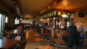 Een restaurant interieur met houten tafels en stoelen, een bar en een televisie aan de muur.