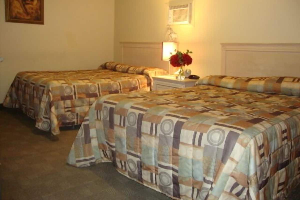 Una habitación de hotel con dos camas, una mesita de noche, una lámpara y un cuadro en la pared.