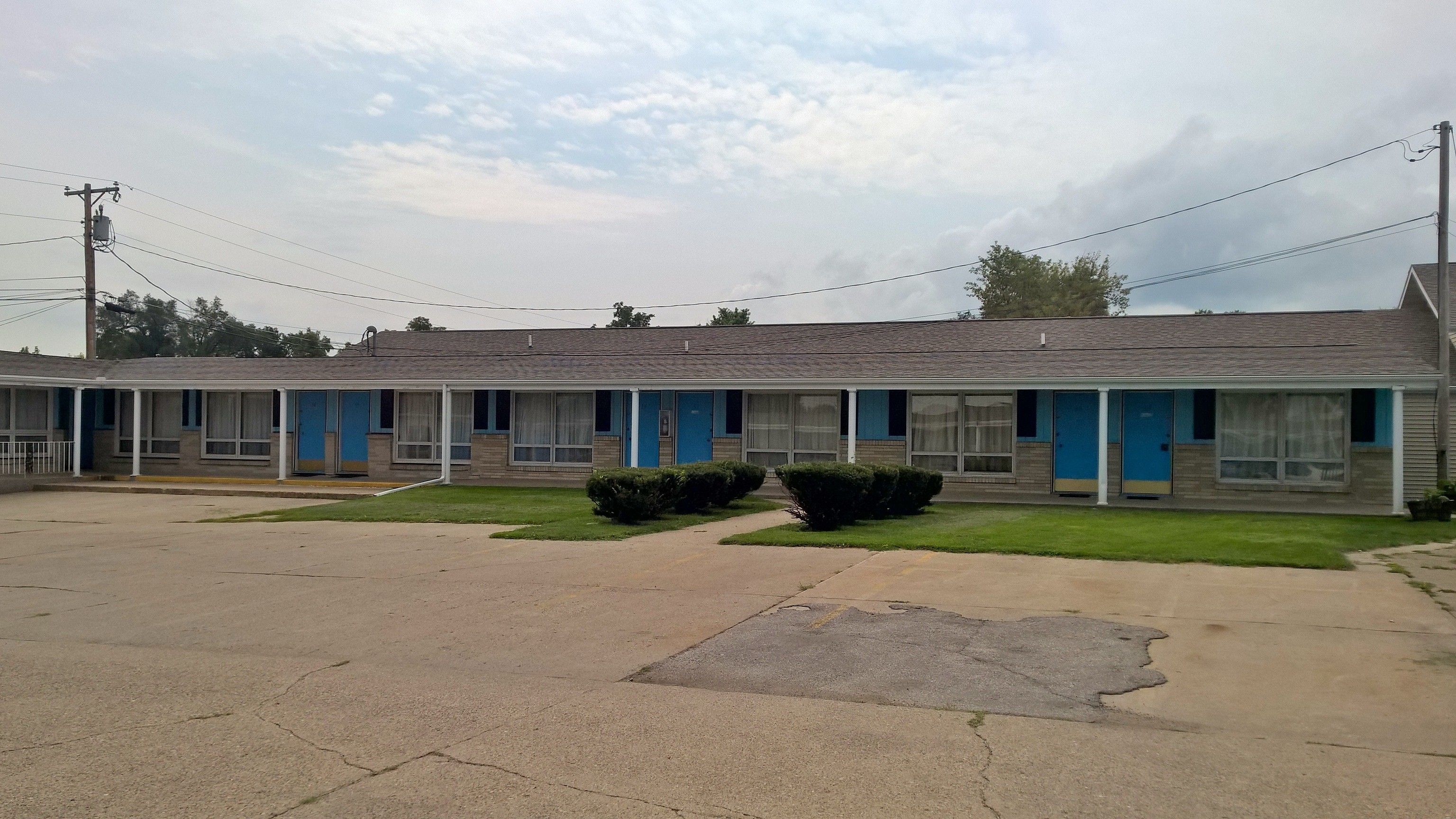 A motel with a row of rooms, each with a blue door and a small front yard.
