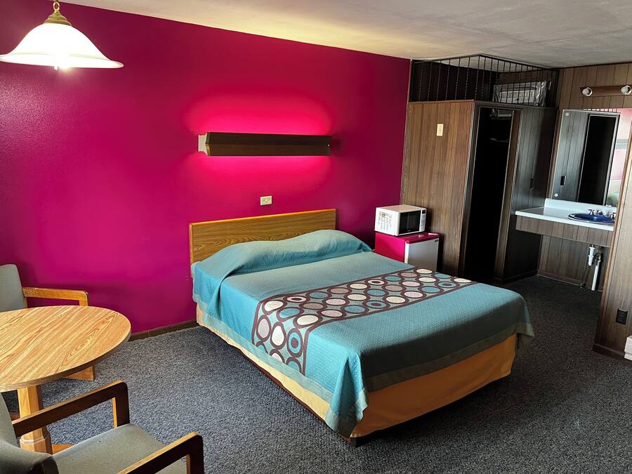 Una habitación de hotel con una cama, una mesita, una silla, un microondas y un lavamanos.