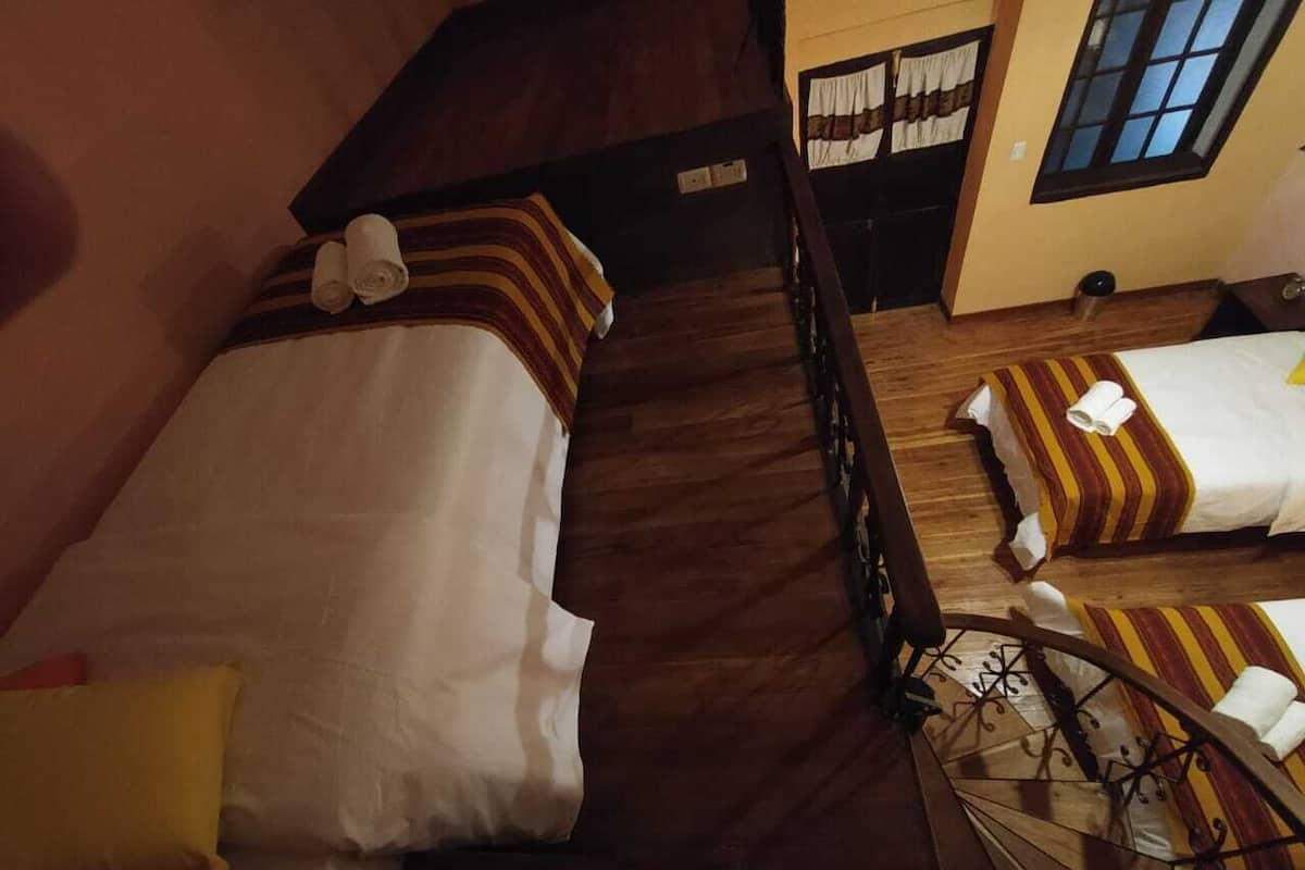 A room with two beds, wooden flooring, and a window.
