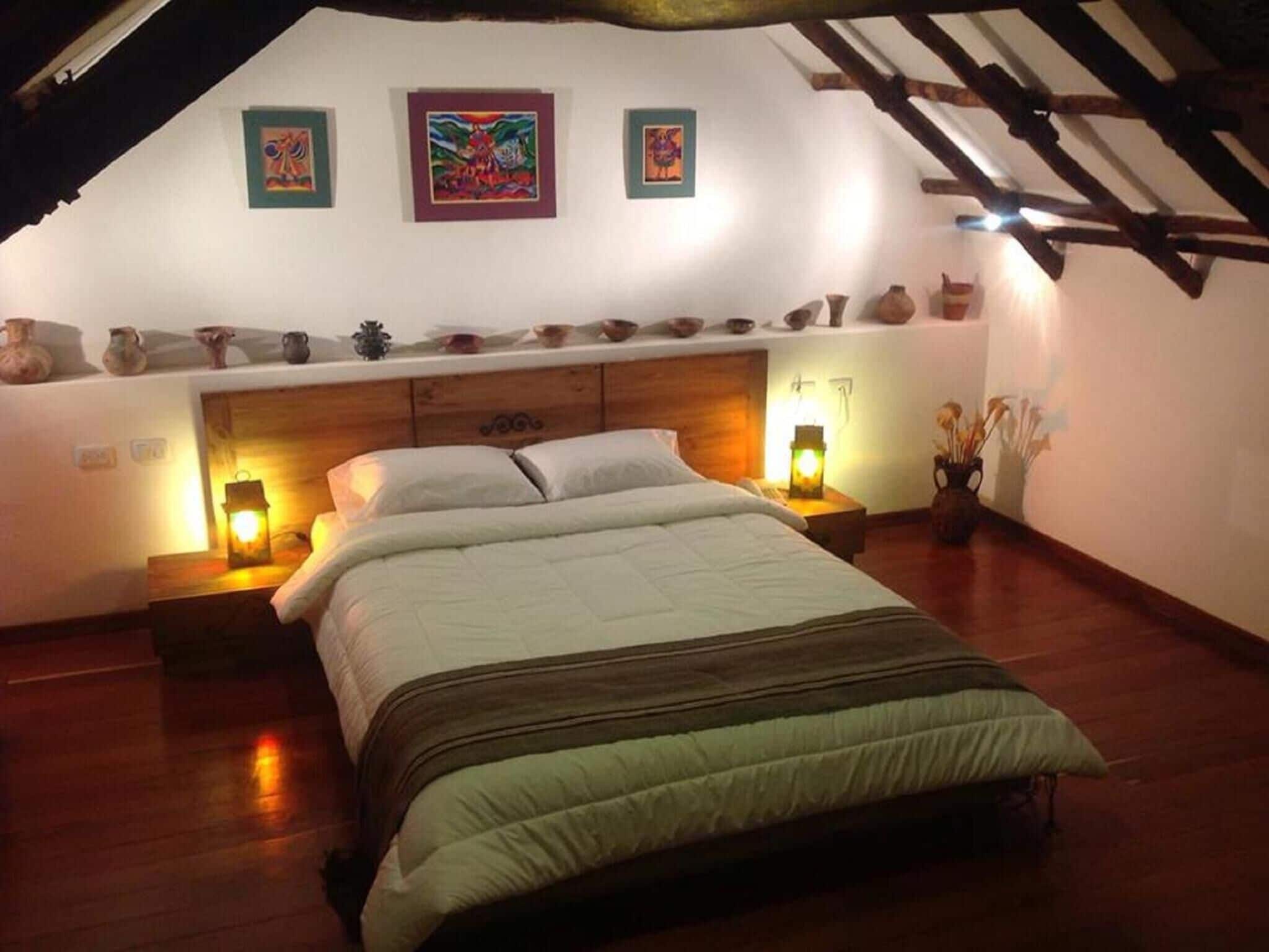 A bedroom with a wooden bed, two bedside lamps, a shelf with pottery, and a sloped ceiling.