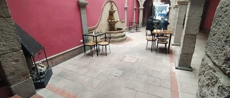 An outdoor courtyard with stone flooring, a fountain, and several tables and chairs.