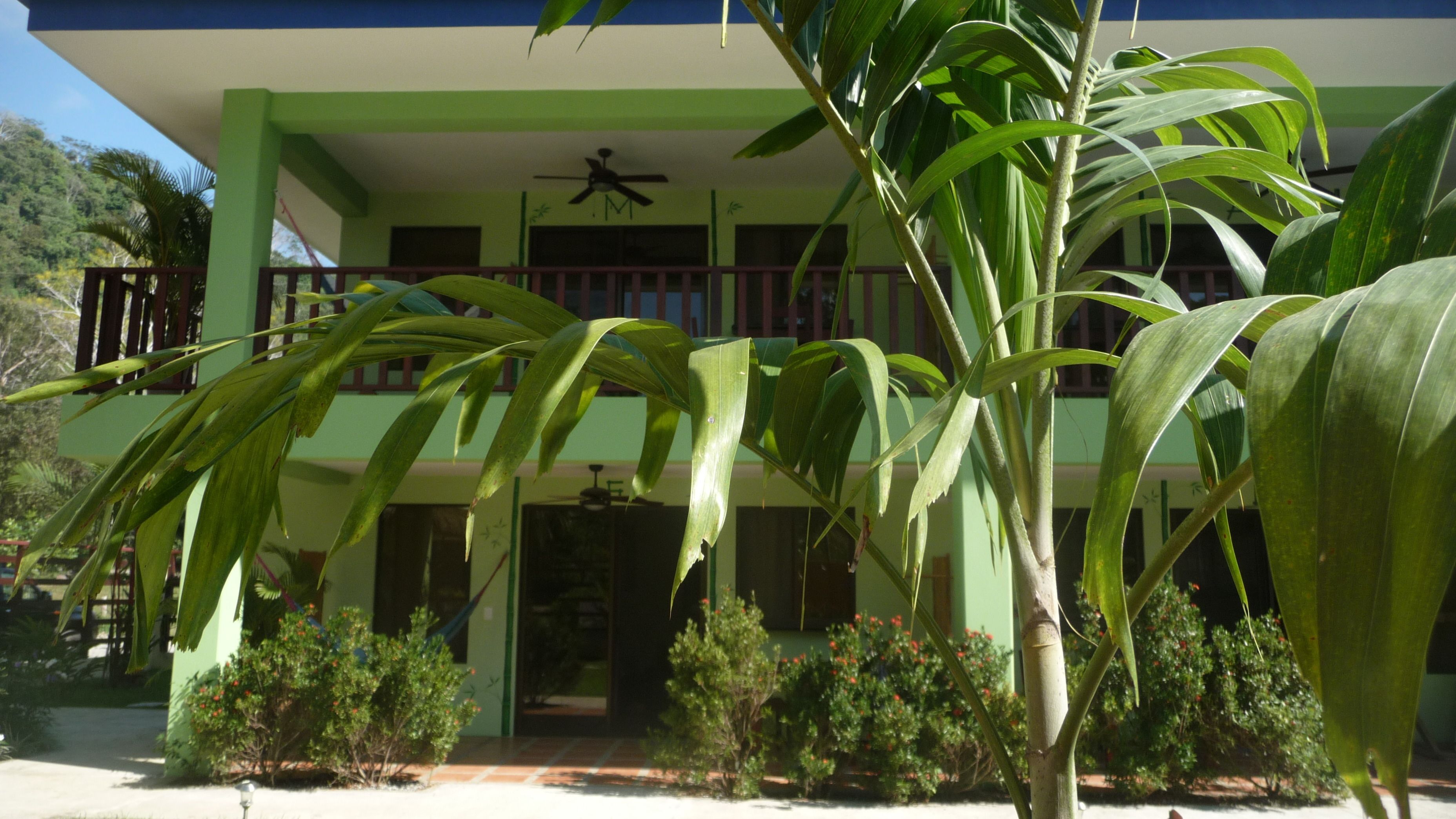 A two-story building with a green and blue exterior, a balcony with a railing, and a ceiling fan.