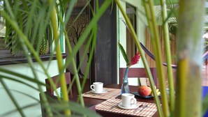 Un comedor con una mesa dispuesta para dos personas, con un jarrón con una flor roja, un plato de fruta y dos tazas.