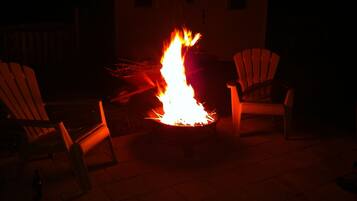 A fire pit with two Adirondack chairs around it, set on a patio with a building in the background.