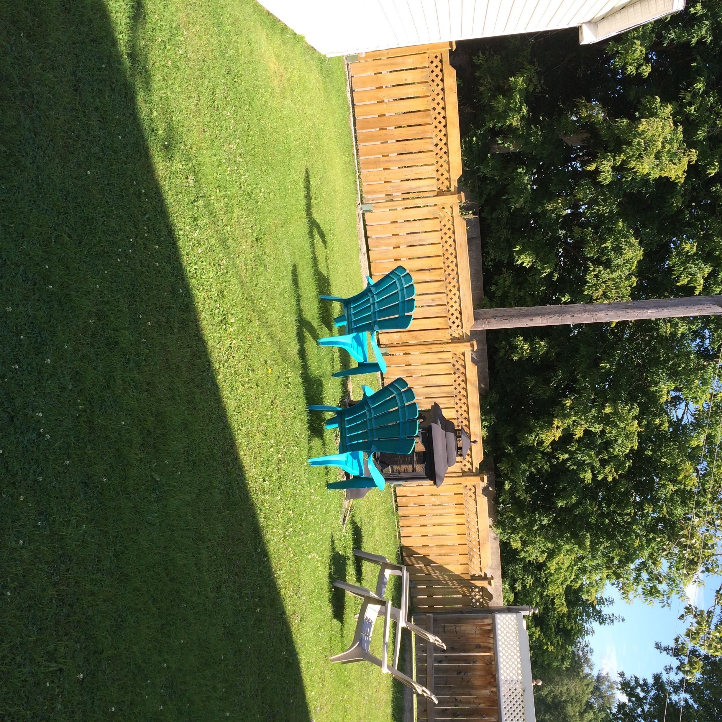 A backyard with a wooden deck, a lawn, and a patio area with a table and chairs.