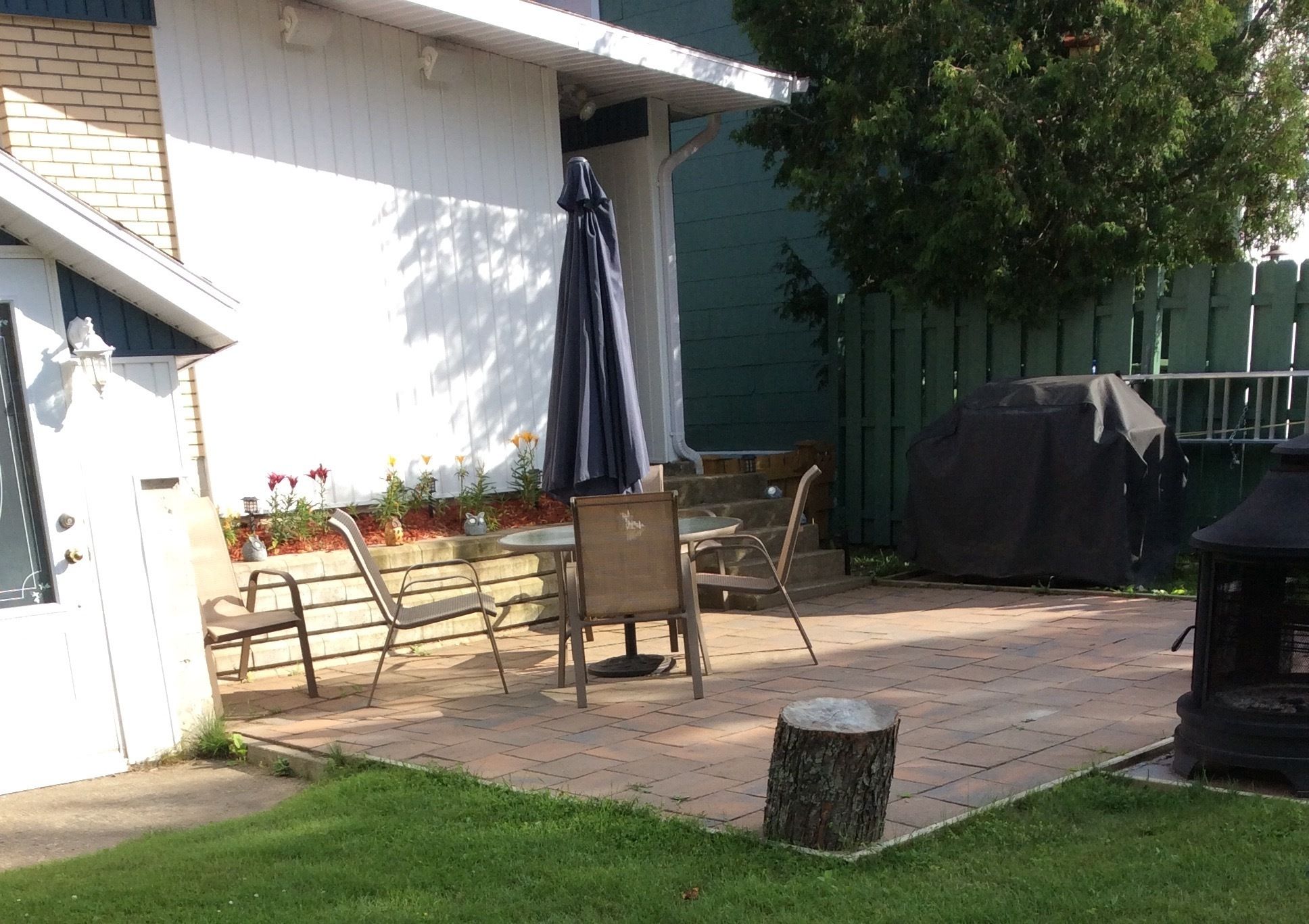 Un patio exterior con un área de estar techada, una parrilla y un tocón pequeño.