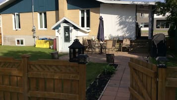 Een terras met buitenmeubilair, een houten omheining en een pad dat naar een gebouw leidt met een groene deur en ramen.