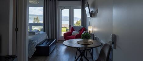 Una habitación moderna con una cama, un sillón rojo, una mesita con una planta y un televisor montado en la pared.