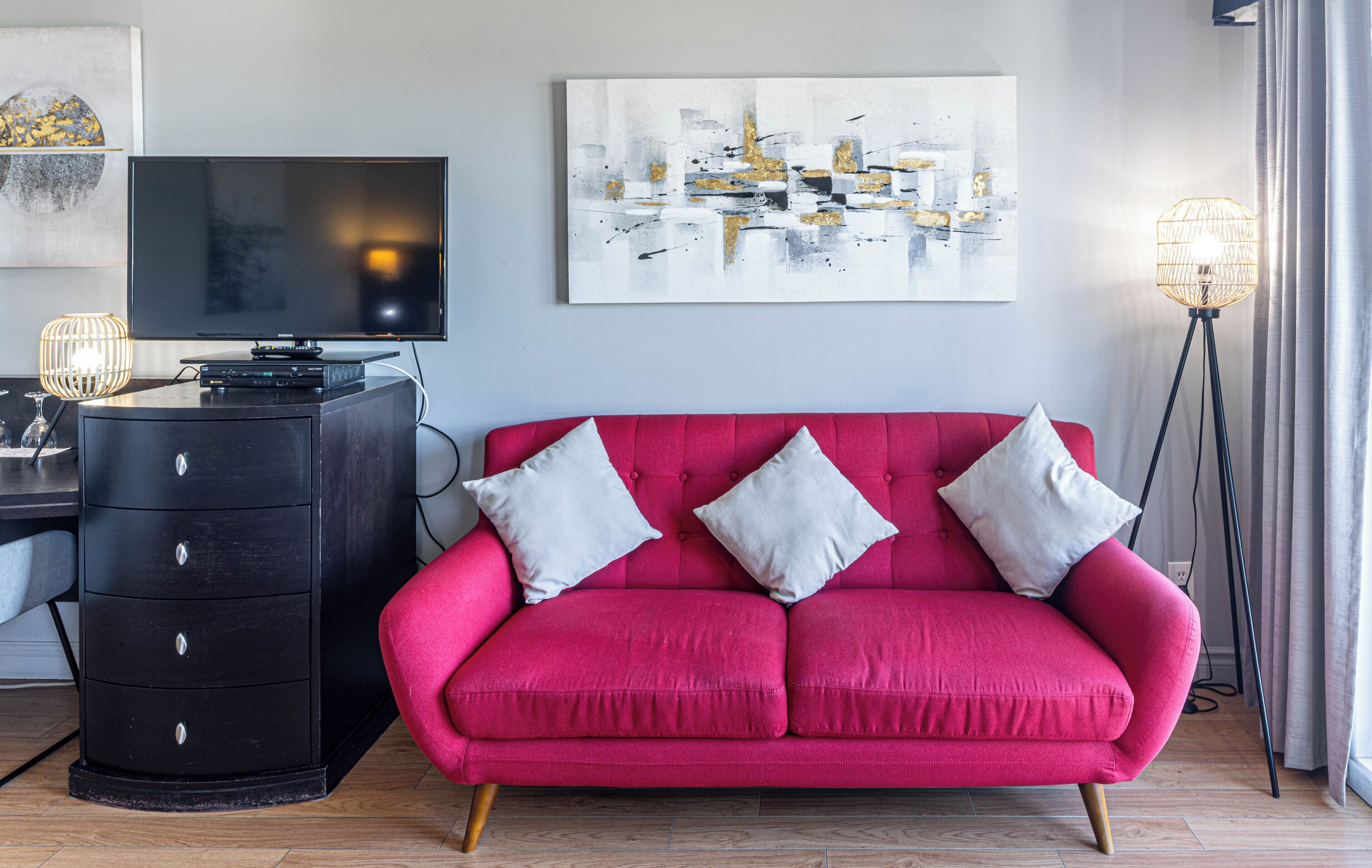 A living room with a red sofa, a black TV stand, and a floor lamp.