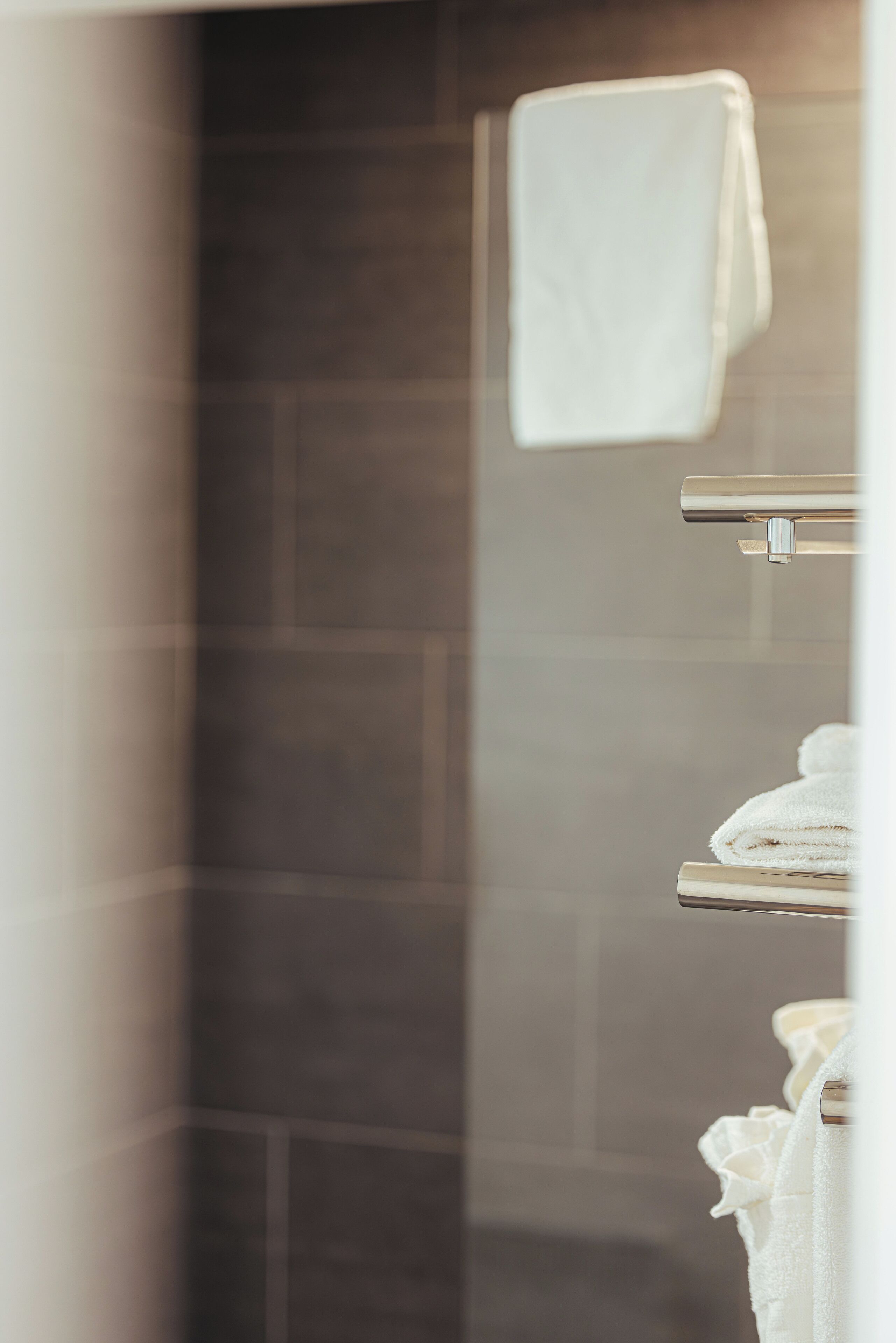 A bathroom with a glass shower enclosure, a towel rack with folded towels, and a tiled wall.