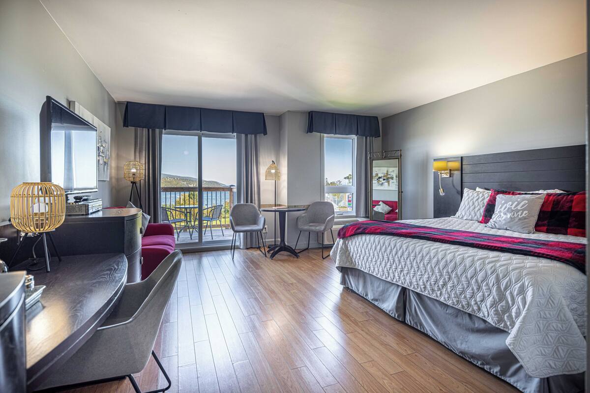 Habitación de hotel con cama, escritorio, dos sillas, una mesita y ventanas amplias.