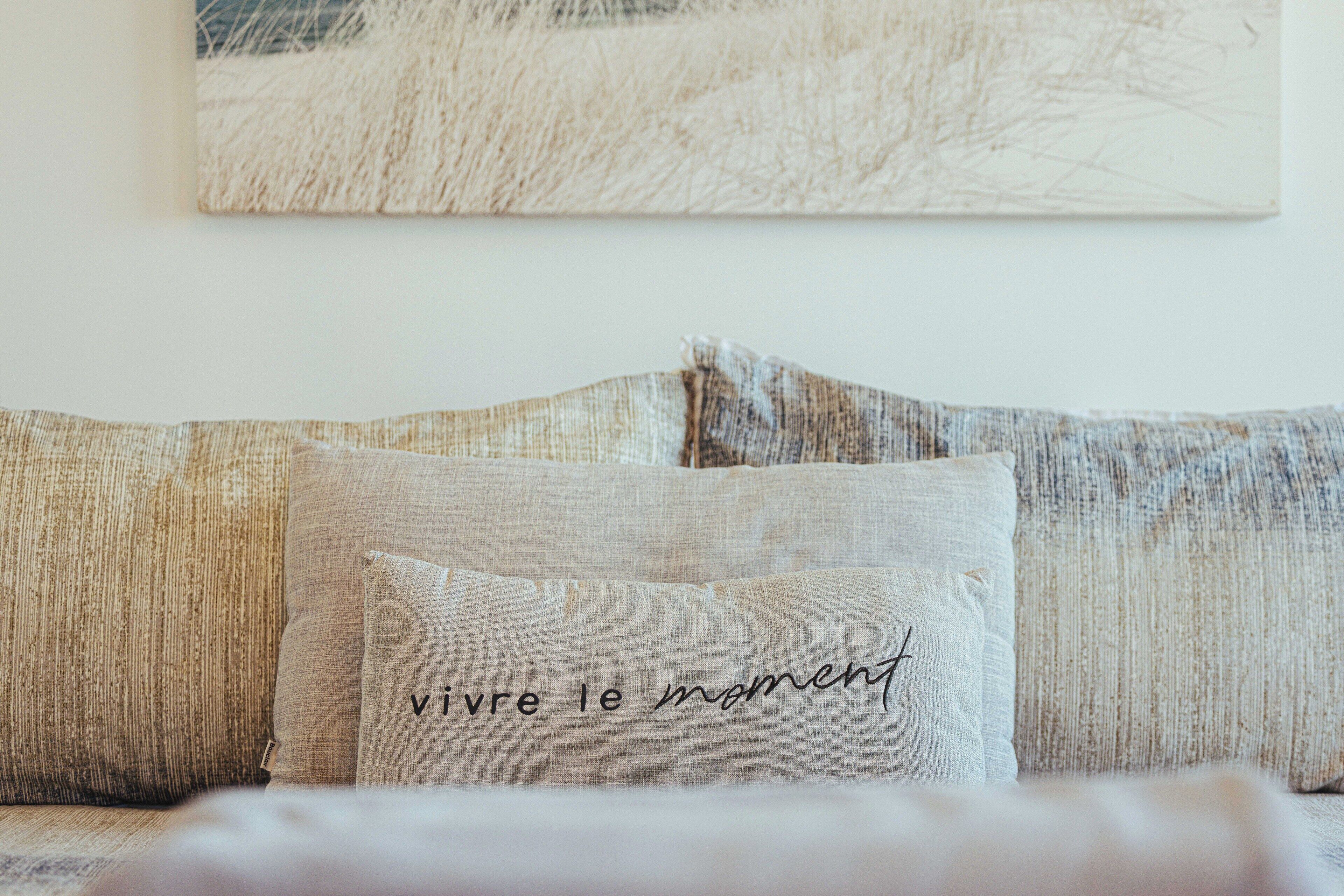Un sofá con un cojín que dice "vivre le moment" y una obra de arte con textura en la pared superior.