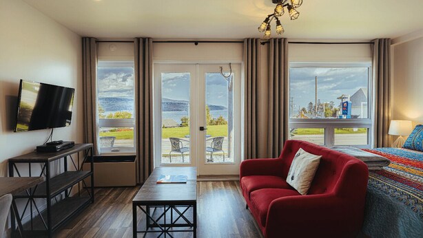 Een moderne kamer met een rode bank, een televisie, een tafel en uitzicht op een groen landschap door grote ramen.