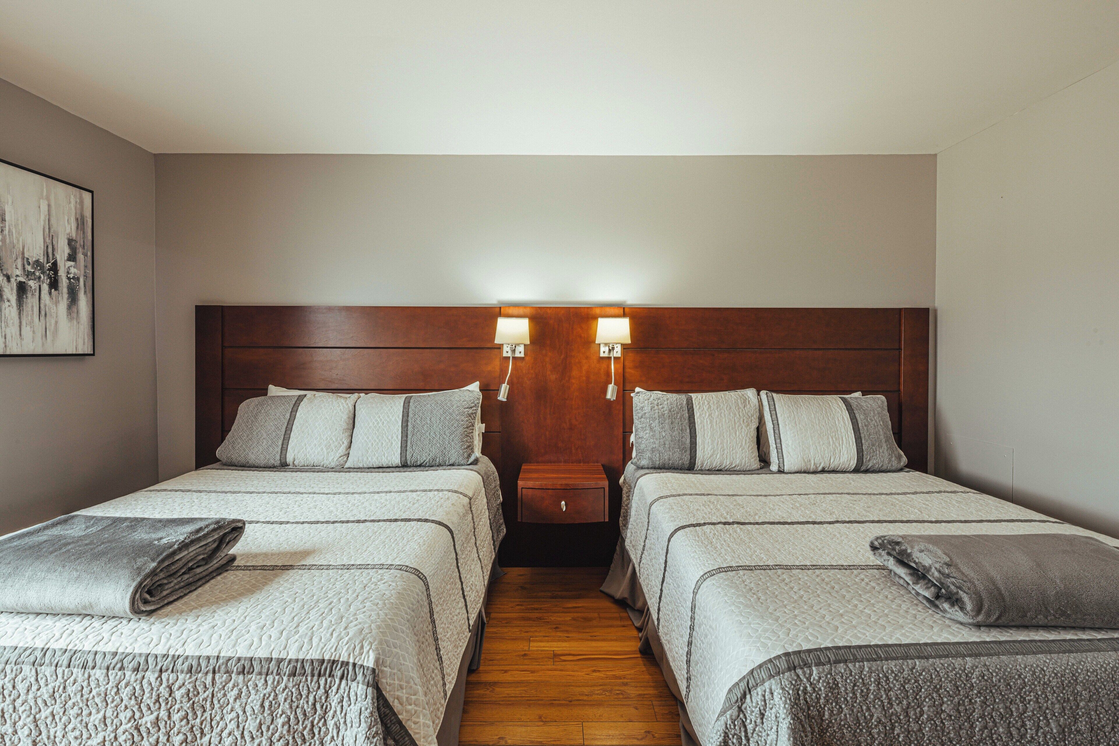 A hotel room with two beds, a wooden headboard, bedside lamps, and a small nightstand.