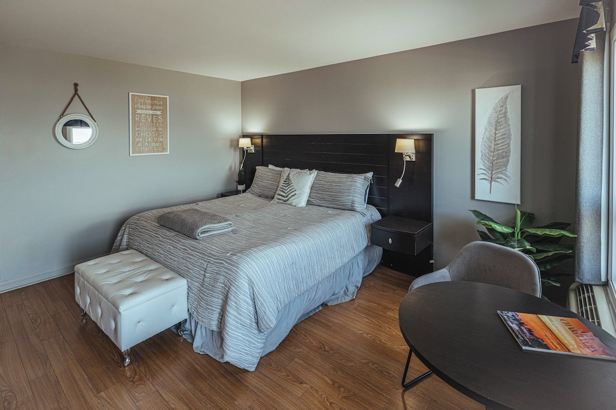 Un dormitorio ordenado con cama, mesitas de noche, una pequeña mesa y una planta en maceta.