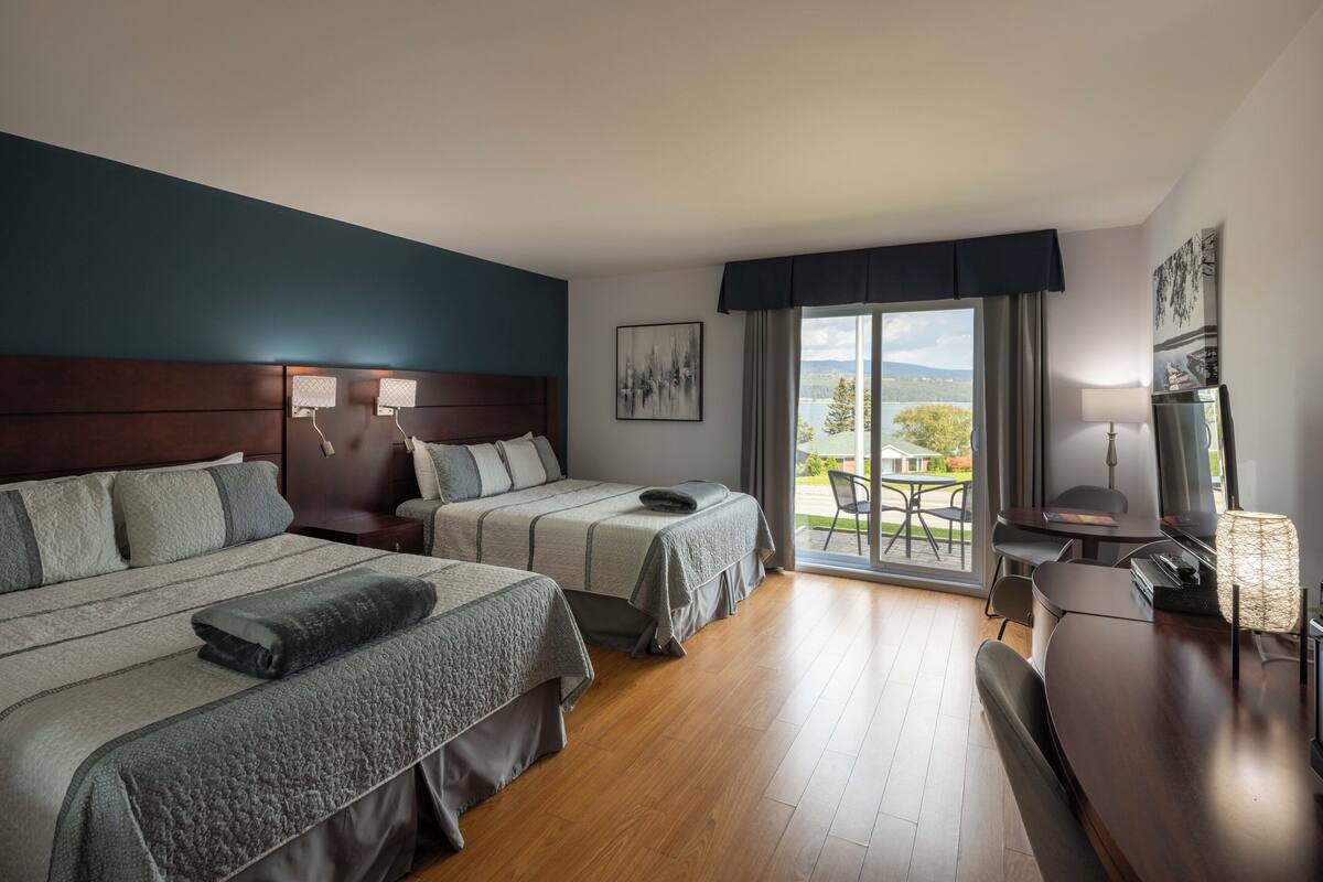 Habitación de hotel con dos camas, un escritorio y vistas al exterior.