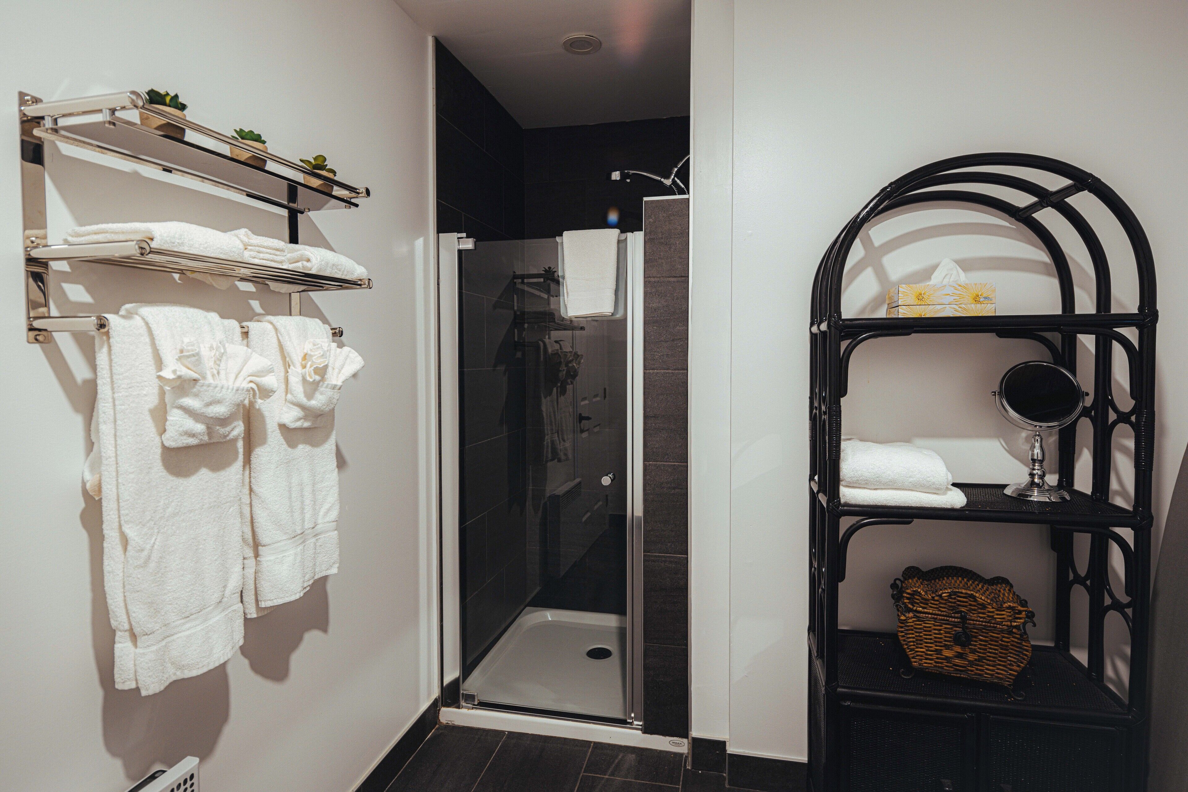 Un baño moderno con ducha envuelta en vidrio, toallas blancas en estantes y un tocador negro con espejo.