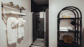 Un baño moderno con ducha envuelta en vidrio, toallas blancas en estantes y un tocador negro con espejo.
